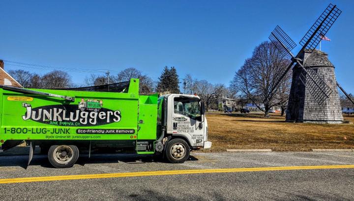 A green truck on the side of a road with a windmill in the background