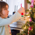 Little Girl Hanging An Ornament On A Christmas Tree