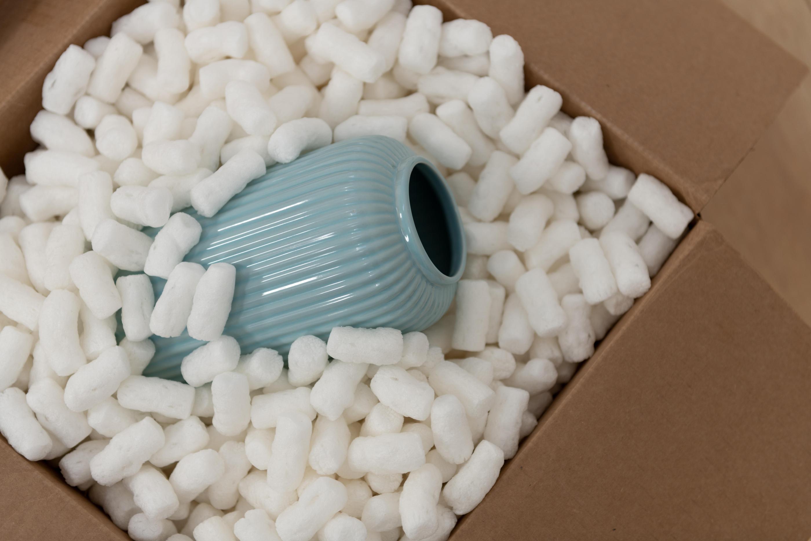 Box of packing peanuts holding a light blue vase